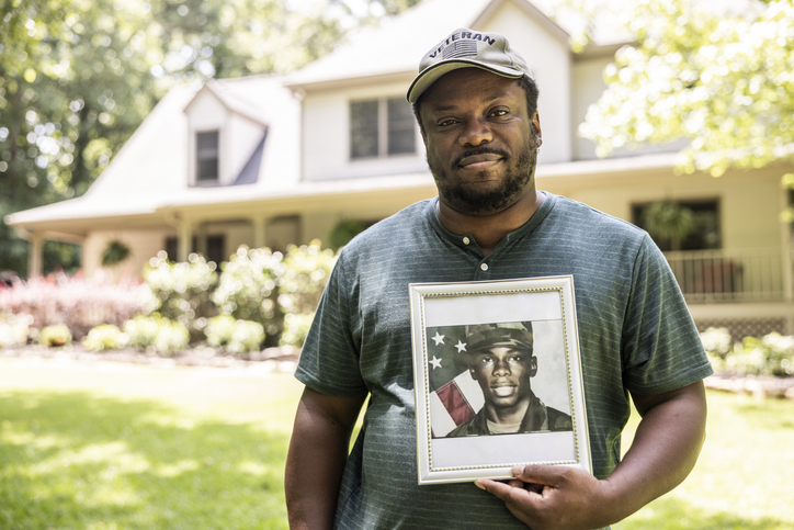Portrait of U.S. military veteran holding framed service portrait in front of home